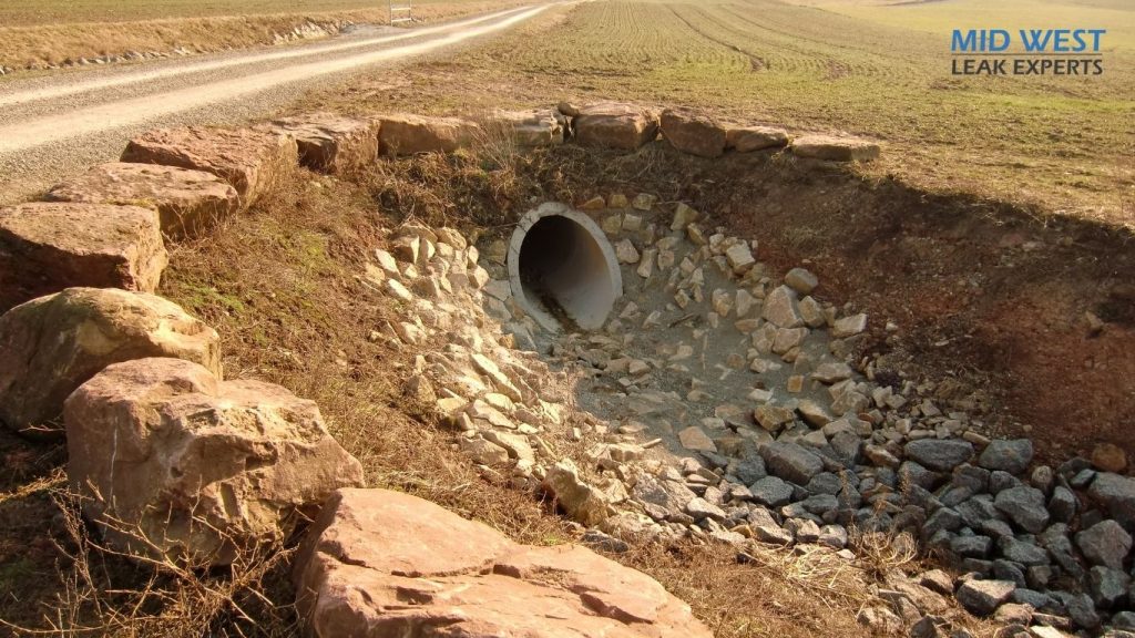 a large stormdrain in the side of a road in the middle of a field