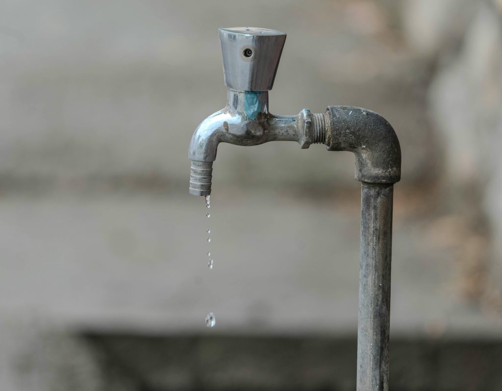 Close-up image of an outdoor water tap with a single droplet falling, highlighting water conservation.